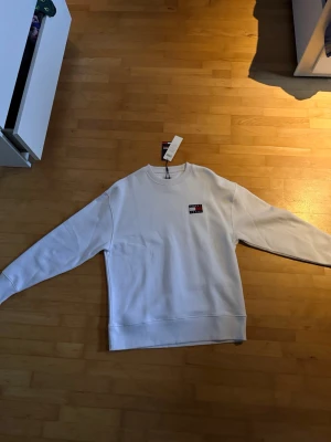 Tommy Hilfiger Tröja Vit – Helt Ny med Tags – Strl M - Vit Tommy Hilfiger tröja i storlek M i absolut nyskick. Aldrig använd och etiketten sitter fortfarande kvar. Stilren och tidlös modell med den ikoniska Tommy Hilfiger-loggan på bröstet som ger en clean och exklusiv look. Perfekt både till vardags och för en mer uppklädd outfit. Ett riktigt bra kap för dig som vill ha en fräsch premiumtröja till ett bättre pris än i butik.