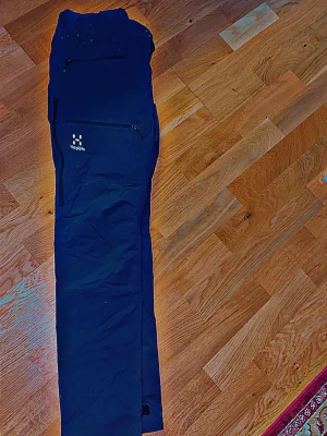 Svarta täckbyxor från Haglöfs - Säljer ett par svarta täckbyxor från Haglöfs med dragkedjeförsedda fickor och justerbara benslut. Perfekta för kalla dagar och outdoor-äventyr. Snygg, enkel design med diskret logga på benet. Materialet är slitstarkt och vindtätt.  Riktigt bra skicka väl omhändertagna unisex tjejen använt ibland 