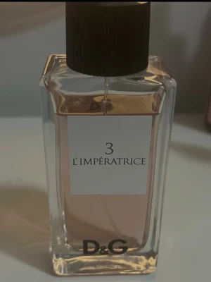 D&G 3 L'Impératrice parfym - D&G 3 L'Impératrice är en elegant parfym i en rektangulär glasflaska med svart kork. Doften har en ljusrosa ton och flaskan har en stilren etikett med svart text. Perfekt för dig som gillar exklusiva och fräscha dofter.