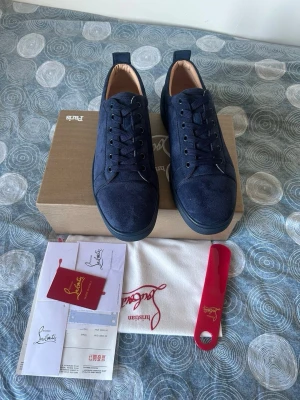 Mörkblå sneakers från Christian Louboutin - Snygga mörkblå sneakers från Christian Louboutin i mocka med klassisk röd sula och svarta snören. Låg modell med diskret logga och stilren design. Kommer med originalkartong, dustbag och tillbehör.