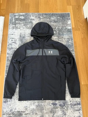 Under Armour Windbreaker  - Säljer denna Under Armour windbreaker/vindjacka eftersom den inte är min storlek. Den är nyligen köpt och är i nytt skick, Aldrig använts och är mycket fin. Priset kan gärna diskuteras!