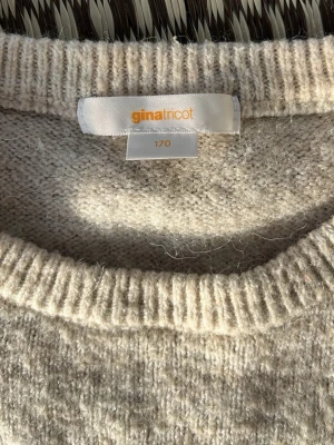 Beige stickad tröja Gina Tricot - Mysig beige stickad tröja från Gina Tricot med rund halsringning och långa ärmar. Tröjan har en enkel och klassisk design med ribbstickade muddar vid hals, ärmslut och nederkant. Perfekt för lager-på-lager och chill dagar.