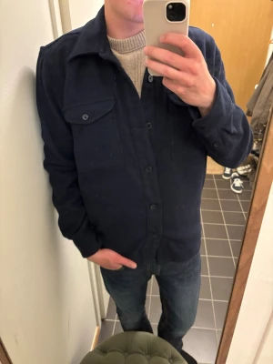 Mörkblå overshirt från Dressmann - Snygg mörkblå overshirt från Dressmann med klassisk krage och knäppning framtill. Bröstficka med lock och knapp, perfekt att slänga över en tröja. Stilren och enkel att matcha till jeans eller chinos.