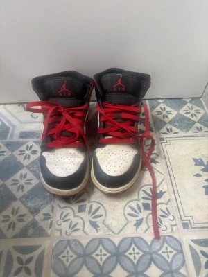 Svarta och vita Air Jordan 1 med röda detaljer - Säljer ett par klassiska Air Jordan 1 sneakers i svart, vitt och rött. 