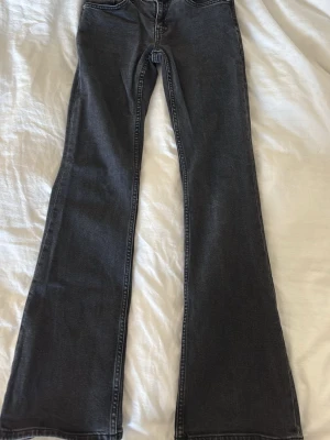 Svarta bootcut jeans med utsvängda ben - Snygga svarta bootcut jeans med utsvängda ben och klassiska fickor både fram och bak. Jeansen har en stilren look med kontrastsömmar och passar perfekt till en trendig vardagsstil. Materialet är denim med lite stretch för extra komfort.