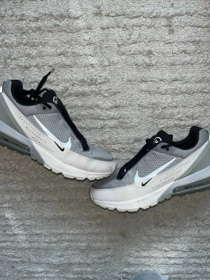Nike Air Max 270 grå sneakers - Nike Air Max 270 sneakers i grått och vitt med svart detalj. Skorna har en luftig mesh-överdel, synlig Air Max-dämpning i hälen och klassisk Swoosh-logga på sidorna. Perfekta för dig som gillar sportig och modern stil.