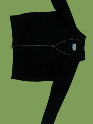 Svart ziptröja från Maison Margiela - Säljer en svart ribbstickad ziptröja från Maison Margiela. Tröjan har hel dragkedja framtill, lång ärm och de ikoniska vita sömmarna i nacken. Perfekt för dig som gillar minimalistisk och stilren design.