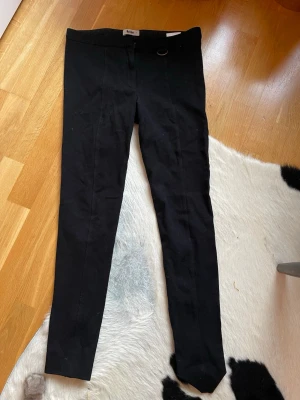 Svarta byxor från Acne med dragkedja bak i storlek 36 - Säljer ett par svarta byxor från Acne med smal passform och dragkedjor längst ner på baksidan av benen. Storlek 36. De har hög midja och en stilren look, perfekta till många olika outfits. Materialet är stretchigt och bekvämt.