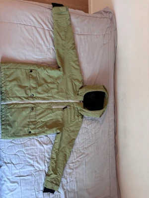 Ljusgrön barn jacka från Club Cprs 158/164 - Snygg ljusgrön parkas från Club Xprs med huva och svarta detaljer. Jackan har dragkedja framtill, två stora fickor med knappar och en bröstficka med dragkedja. Fodrad insida i svart och justerbara ärmslut. Perfekt för kyliga dagar.