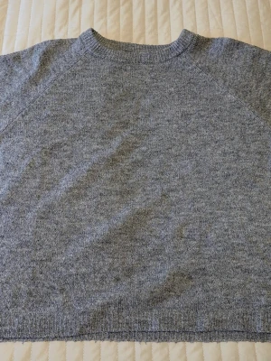 Grå stickad tröja från 157 - Mysig grå stickad tröja från 157 med rund halsringning och ribbade muddar. Tröjan har en enkel och stilren design som passar perfekt till lager-på-lager och är lätt att matcha med olika outfits.