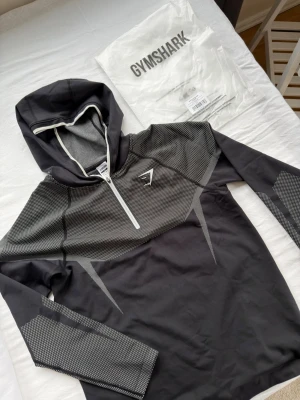 Svart Gymshark Onyx hoodie XL - Snygg svart hoodie från Gymshark med halv dragkedja framtill och vit logga på bröstet. Storlek XL och helt oanvänd. Kommer i original  förpackning. Snabb leverans. Skickas samma dag.
