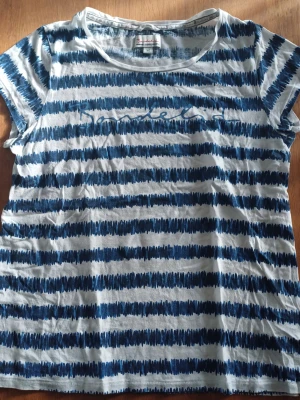 Randig blåvit t-shirt från Bondelid - Säljer en blåvit t-shirt från Bondelid med handritade ränder och tryckt text på bröstet. T-shirten har rund halsringning och korta ärmar. Tillverkad i mjuk bomull som känns skön mot huden. Perfekt för en avslappnad och stilren look.