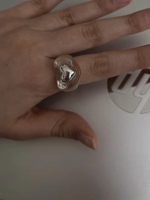 Chunky silverfärgad statementring - Säljer en chunky statementring i silverfärgad metall med organisk, vågig form. Ringen har en blank yta som reflekterar ljuset och ger en modern, edgy vibe. Perfekt för dig som gillar unika accessoarer som sticker ut. Säljer den pga att jag använder den inte längre pga att ringen är inte min stil.