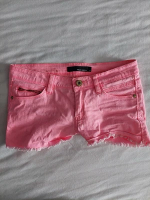 Rosa shorts från Tally Weijl - Säljer ett par ljusrosa shorts från Tally Weijl i klassisk femficksmodell. De har råa kanter nertill och knappgylf. Perfekta för varma dagar och ger en fräsch look till din outfit.