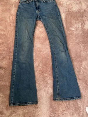 Blå bootcut jeans från Gina Tricot - Säljer ett par klassiska blå bootcut jeans från Gina Tricot. Jeansen har fem fickor, normalhög midja och utsvängda ben. Tillverkade i slitstark denim med snygga detaljer vid fickorna och gylf med dragkedja och knapp. De har även lite fläckar som jag tror inte går bort, se bild 3 och 5💕💕