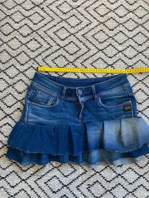 Volangkjol i denim från G-Star RAW - Säljer en snygg jeanskjol från G-Star med volangkant och slitna detaljer. Cool färg på tyget. Omsydda jeans. Perfekt till sommaren!