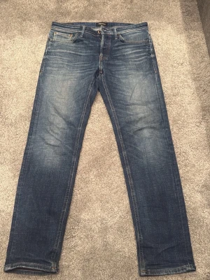  Jack & Jones jeans   - Snygga blå jeans från Jack & Jones med klassisk femficksmodell och raka ben. Jeansen har en tvättad look med slitningar och kontrastsömmar. Perfekta för en avslappnad och trendig stil. Materialet är denim i bomull.  Storlek 32/32