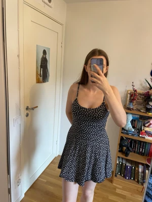 Svart klänning med vita blommor  - Söt svart klänning med vita små blommor och smala axelband. Den slutar över knäna och är utmärkt att ha en varm sommardag 
