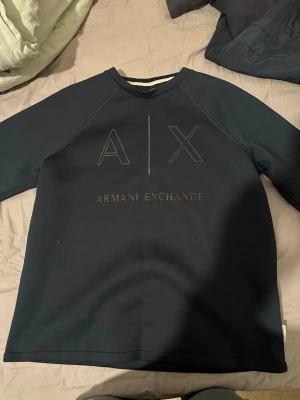 Svart sweatshirt från Armani Exchange - Stilren svart sweatshirt från Armani Exchange med stort A|X-tryck och logga framtill. Tröjan har rund halsringning och långa ärmar. Perfekt för en avslappnad och trendig look. EJ ANVÄND‼️ Snabbaffär 350kr