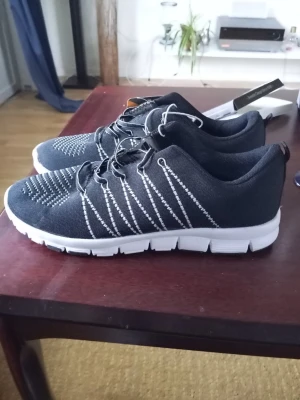 Svarta sneakers med vit sula - Säljer ett par svarta sneakers med vit sula och vita detaljer i stickningen. Skorna har en sportig look med lågt skaft och snörning. Ovandelen är i textilmaterial som andas och sulan är lätt och flexibel. Perfekta för dig som gillar stilrena och bekväma skor.
