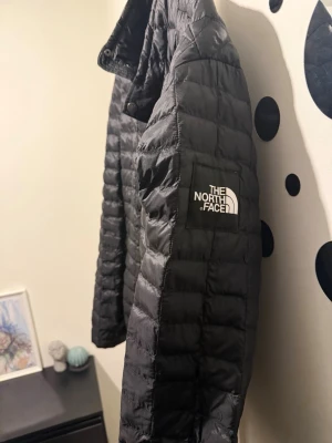 Svart dunjacka från The North Face XL - Snygg svart dunjacka från The North Face i storlek XL. Jackan har quiltad design, hög krage och logga på bröstet. Perfekt för kalla vinterdagar och riktigt lätt att bära. Klassisk modell som funkar till det mesta.