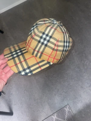 Beige keps med rutigt mönste - Använd ett pat gånger men helt okej stick och den kan justeras där bakom 