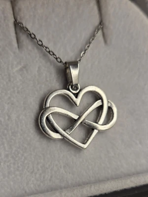 Halsband med hjärta och evighetssymbol - Snyggt halsband i rostfritt stål med ett hänge som kombinerar ett hjärta och en evighetssymbol. Kedjan är 45 cm, tunn och klassisk, perfekt för att ge en stilren touch till din outfit. 
