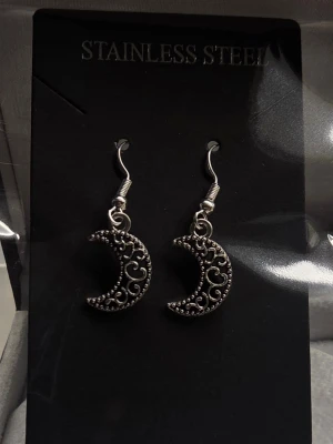 Måneformade örhängen i stål - Snygga örhängen i rostfritt stål med måneformad design och detaljerade mönster. De har en antik silverfärg och hängande krokfäste. Perfekta för dig som gillar unika accessoarer med lite mystisk vibe. Ca 1,5 - 2 cm långa.