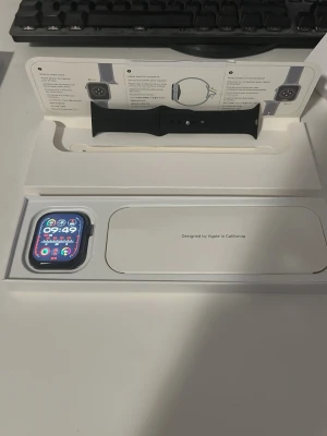 Apple Watch series 9 - Apple Watch med svart sportband och fyrkantig aluminiumboett. Klockan har en färgstark Retina-skärm och levereras i originalförpackning med instruktioner. Obs! Klockan är inte en äkta Apple Watch men har ungefär samma funktioner. Perfekt för dig som vill ha koll på notiser, hälsa och träning direkt på handleden.