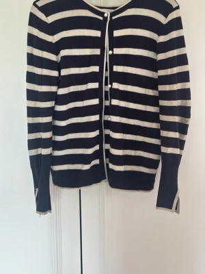 Randig kofta från Zara, marinblå/vit - Snygg kofta från Zara i marinblått och vitt med horisontella ränder. Rund halsringning och pärlknappar framtill. Långärmad modell i mjukt, tunt material som passar perfekt till lager på lager. Klassisk och stilren design.