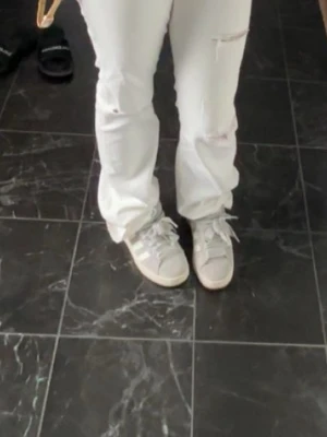 Vita raka jeans med slitningar - Säljer ett par vita jeans med raka ben och slitningar vid knäna. Jeansen har en avslappnad passform och är perfekta för en trendig och casual look. Materialet är klassisk denim och färgen är helt vit.