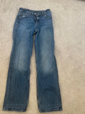 Blå raka jeans från ZARA - Säljer ett par klassiska blå jeans från ZARA i rak modell. Jeansen har fem fickor, normal midja och subtila slitningar för en avslappnad look. Tillverkade i bomull med snygg tvättad finish. Perfekta till en trendig vardagsstil.
