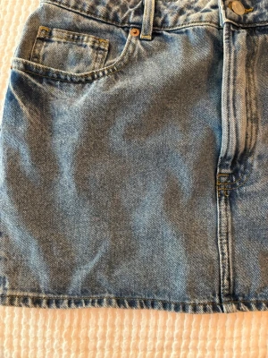 Blå jeanskjol från H&M, storlek 40 - Säljer en klassisk blå jeanskjol från H&M i storlek 40. Kjolen har femficksmodell, knapp och dragkedja framtill samt bälteshällor. Perfekt basplagg i garderoben och lätt att matcha med olika stilar.