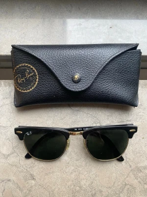 Ray-Ban Clubmaster solglasögon svart/guld - Snygga Ray-Ban Clubmaster solglasögon med svart ovandel och guldfärgade detaljer. Klassisk retroform med mörka glas och tunna metallbågar. Kommer med original svart fodral i skinnimitation med Ray-Ban-logga. Perfekt accessoar för en cool look. Skicka bud! 