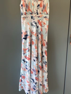 Långklänning från Stockh LM i pastell - Långklänning från Stockh LM med abstrakt mönster i pastellfärger som rosa, blått och vitt. Klänningen har ärmlös design och mjukt, flytande tyg som ger en elegant siluett. Perfekt för sommarens alla tillfällen.