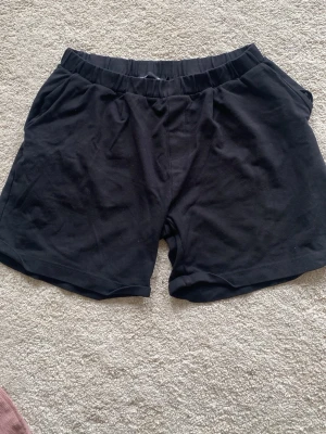 Svarta shorts i bomull med resårmidja - Säljer ett par svarta shorts med elastisk midja och avslappnad passform. Tillverkade i mjuk bomull, perfekta för varma dagar eller chill hemma. Klassisk design utan synliga detaljer eller mönster. Fynda mer och spara på frakten 