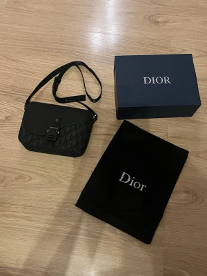 Svart  handväska - Snygg svart handväska med justerbar axelrem i tyg. Kommer med original dustbag och box.