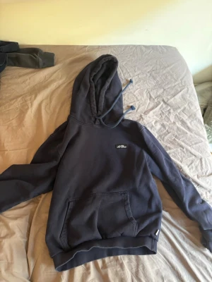 Mörkblå hoodie från Les Deux - Mörkblå hoodie från Les Deux med broderad logga på bröstet. Klassisk känguruficka framtill och justerbar huva med dragsko. Tillverkad i mjuk bomullsblandning som känns skön mot huden. Perfekt för en avslappnad och stilren look.