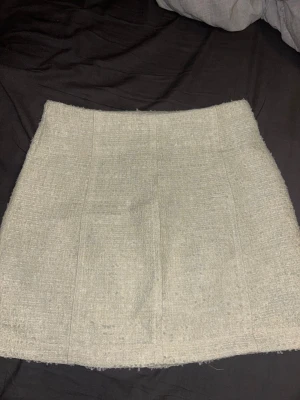 Vit kortkjol från Zara - Säljer en vit kortkjol från Zara i ett strukturerat tyg som ger en trendig och stilren look. Kjolen har råa kanter och en enkel, rak passform som är lätt att matcha med olika outfits.