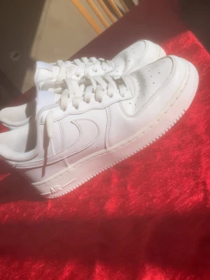 Nike Air Force 1 vita sneakers - Klassiska helvita Nike Air Force 1 sneakers i lågt utförande. Skorna har en stilren design med perforerad tå, kraftig sula och ikoniska Swoosh-loggan på sidan. Tillverkade i läder med vita skosnören och AIR-detalj på sulan. Skorna är använda men jag tar hand om dem bra, dock som alltid händer med air force så har sulan blivit lite gul men de har jag färgat mer högkvalite sko färg 