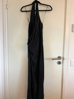 Svart långklänning med tunna band - Svart långklänning med tunna axelband och draperad front. Klänningen har en elegant, lös passform och är tillverkad i ett mjukt tyg som faller snyggt. Perfekt för dig som gillar minimalistisk och stilren design. Aldrig använd. Köpt second hand
