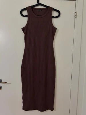 Brun ribbad ärmlös klänning - Säljer en brun, ribbad klänning med tight passform och ärmlös design. Klänningen har rund halsringning och är i stretchigt material som sitter snyggt på kroppen. Perfekt för dig som gillar en enkel men stilren look.
