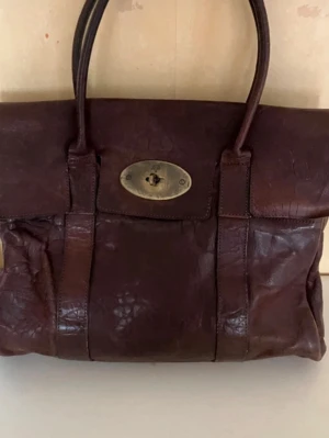 Mörkbrun Mulberry Bayswater väska - Säljer en klassisk Mulberry Bayswater handväska i mörkbrunt läder med krokopräglad struktur. Väskan har dubbla handtag och ett snyggt vridlås i mässing framtill. Perfekt för dig som gillar tidlös och lyxig design.