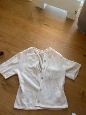 Vit kortärmad kofta Gina Tricot - Söt vit kofta från Gina Tricot i mjuk ullblandning. Kortärmad modell med rund hals och pärlemorknappar framtill. Perfekt att slänga över en topp för en chill och stilren look.
