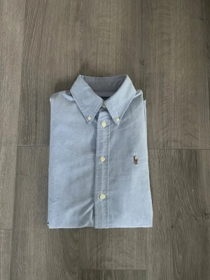 Ralph Lauren skjorta - Säljer nu en ljusblå Ralph Lauren skjorta i storlek Xs. Den är i mycket bra skick och har inga defekter. Stilren skjorta som är enkel att matcha med ett par jeans eller ett par linnebyxor nu till sommaren. Hör av dig vid minsta fundering🤩 Obs! Måtten fick inte plats i bilderna men de är 66cm från toppen till botten och 45 rakt över mätt precis under första knapp.