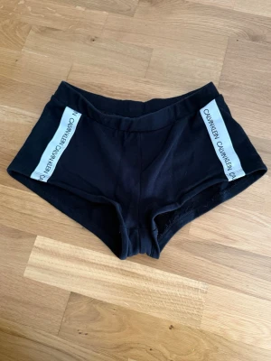 Svarta shorts från Calvin Klein - Svarta shorts från Calvin Klein med vita logoband längs sidorna. Stl. XS