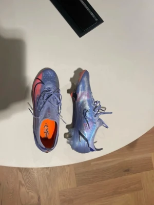 Nike Mercurial fotbollsskor - Säljer ett par Nike Mercurial Elite fotbollsskor i blå och lila nyanser med svarta detaljer och orange insida. Väldigt väldigt bra kvalité. Finns ingenstans och hitta. 