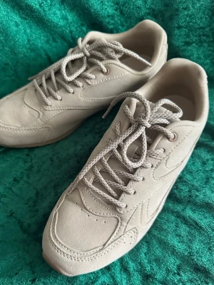 Beige dam sneakers från CLD storlek 39( inte äkta leder) - Stilrena beige sneakers från CLD med snygga sömdetaljer och matchande beige skosnören. Ovandelen är i mockaliknande material och sulan är diskret ton-i-ton. Perfekta för dig som gillar en clean och enkel look.