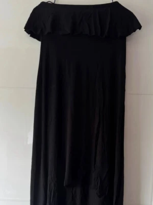 Svart offshoulder långklänning - Säljer en svart långklänning med offshoulder-design och volang upptill. Klänningen har en rak och enkel siluett som ger en stilren look. Perfekt för dig som gillar minimalistisk stil och vill ha något bekvämt men ändå snyggt.