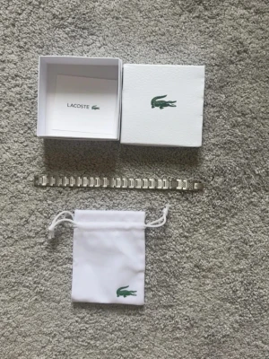 Silverfärgat armband från Lacoste - Snyggt armband i silverfärgad metall från Lacoste med klassisk länkdesign och diskret Lacoste-logga. Kommer med original ask och tygpåse med krokodil-loggan. Perfekt accessoar för dig som gillar stilrena detaljer och vill lyfta din outfit.